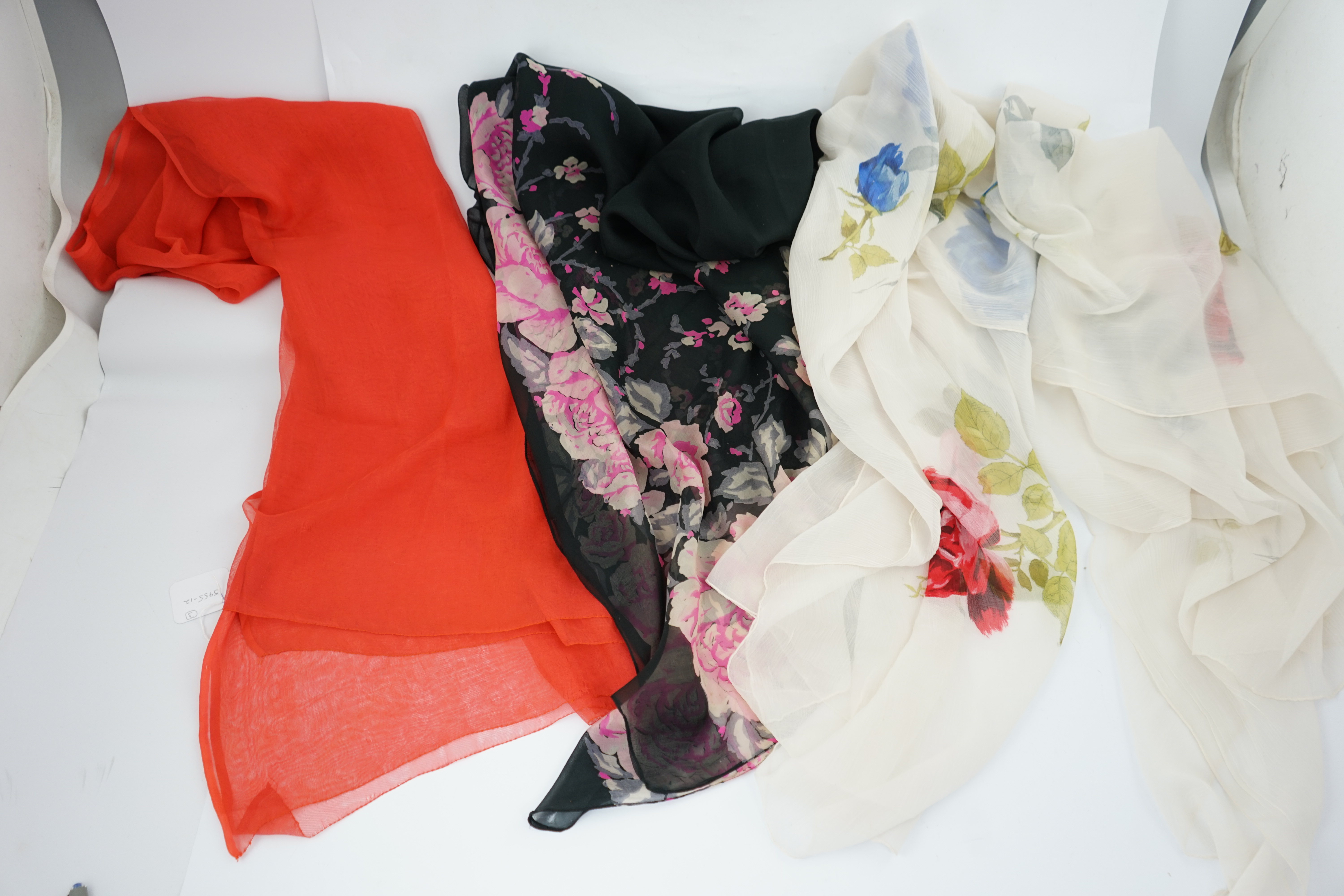 Three 1950s silk chiffon evening stoles, one cream crepe de chine designed with large red and blue single stem roses, another black silk chiffon with wide pink rose border, the other a plain coral chiffon, cream stole 18